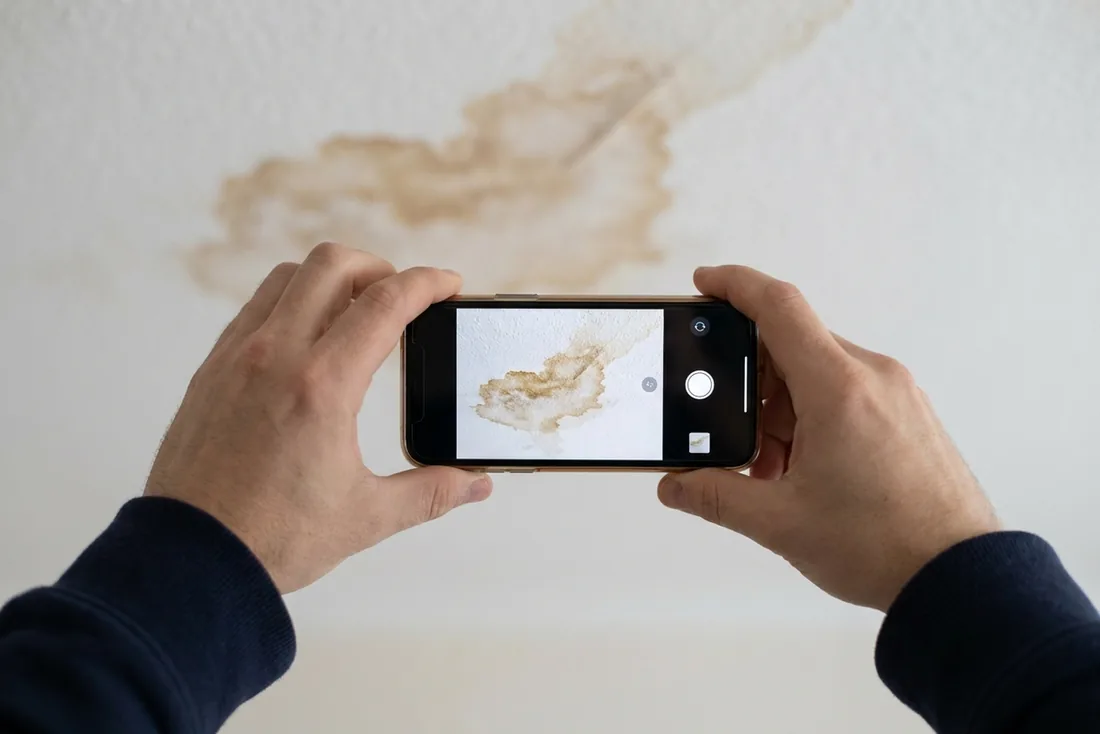 Des mains photographient au téléphone une tache brune sur un plafond blanc